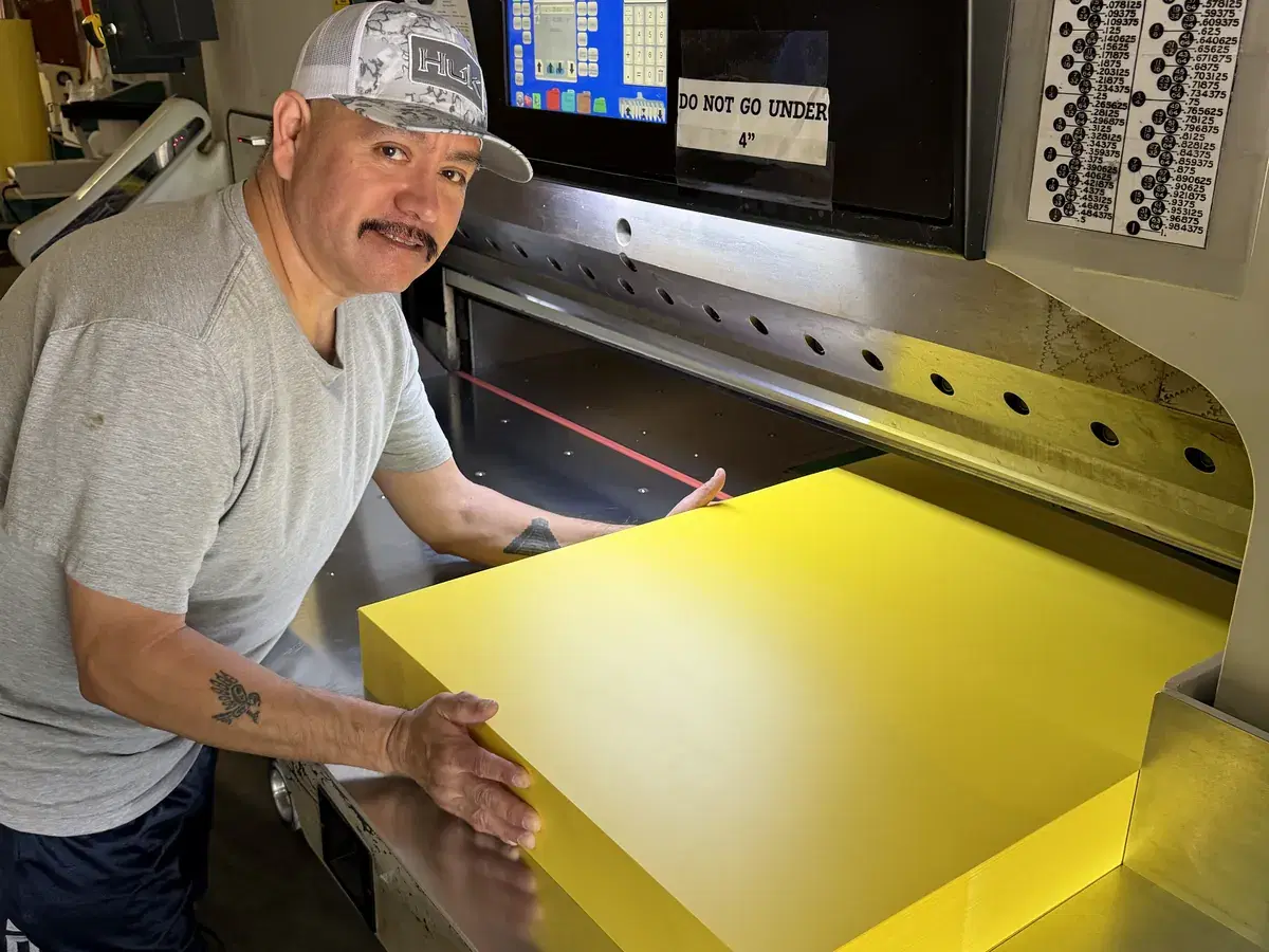 K&R Plastics converting operator squaring a stack of yellow sheet on the guillotine cutter